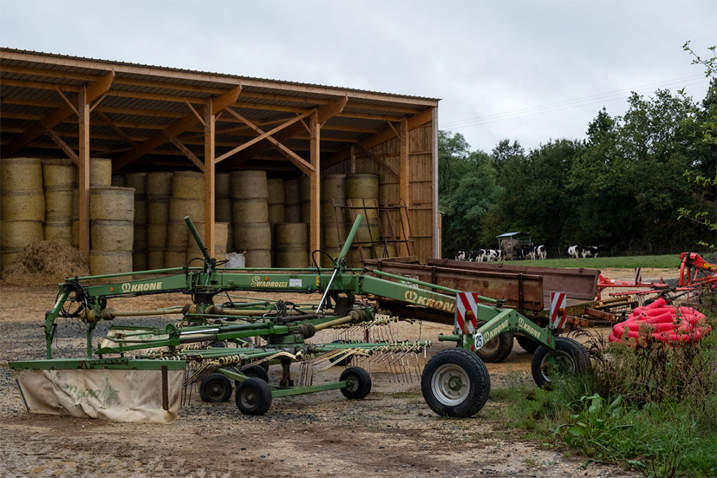 farm tool and hay bales with cows in background